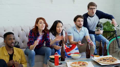 Group-of-young-friends-sports-fans-with-British-national-flags-watching-sport-championship-on-TV-together-and-happy-about-winning-favourite-team-at-home