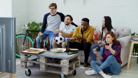 Multi-ethnischen-Gruppe-von-Freunden-Sport-Fans,-die-Fußball-EM-im-Fernsehen-zusammen-Pizza-essen-und-Bier-zu-Hause-beobachten