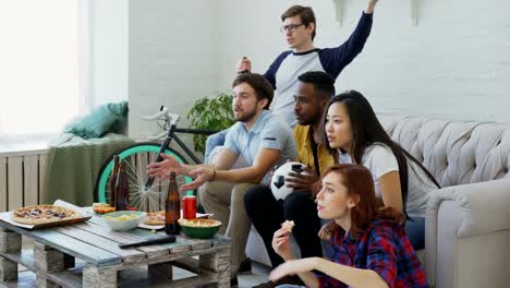 Happy-friends-watching-sports-championship-on-TV-together-at-home-while-eating-snacks-and-drinking-beer-at-home.-They-are-happy-about-winning-of-favourite-team