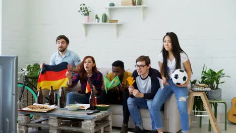 Amigos-jóvenes-viendo-Juegos-Olímpicos-partido-en-TV-juntos-en-casa.-Algunos-de-ellos-contento-con-el-equipo-alemán-en-ganar-pero-hombre-brasileño-decepcionó