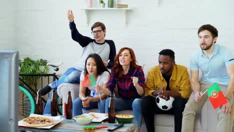 Amigos-felices-con-las-banderas-portuguesas-ver-Campeonato-de-deportes-en-la-TV-en-casa-y-feliz-ganadora-del-equipo-favorito