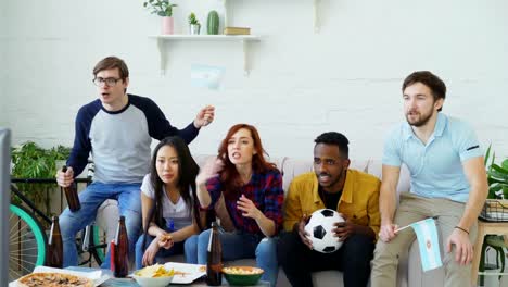 Amigos-felices-con-las-banderas-argentinas-ver-Campeonato-de-deportes-en-la-TV-en-casa-y-feliz-ganadora-del-equipo-favorito