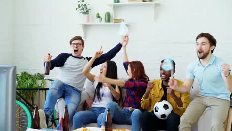 Grupo-multiétnico-de-amigos-deportes-aficionados-con-banderas-argentinas-ver-Campeonato-de-fútbol-en-la-televisión-juntos-en-casa-y-animar-para-arriba-equipo-favorito