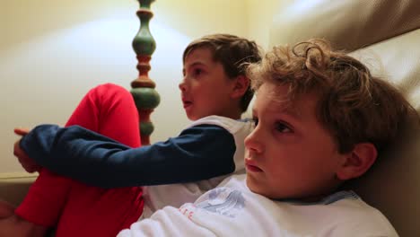 Die-jungen-sitzen-auf-dem-Sofa-vor-dem-Fernseher-hinter-der-Kamera.-4K-candid-Clip-von-Kindern,-die-auf-Bildschirm-zu-Hause