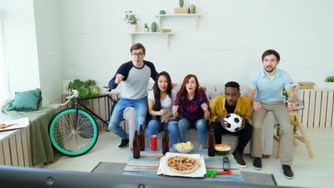 Happy-young-friends-watching-sports-game-on-TV-jumping-and-celebrating-victory-of-favourite-team-at-home