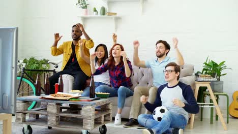 Gruppe-der-happy-Friends-Sportspiel-im-Fernsehen-zu-Hause-beobachten.-Sie-Aufmunterung-Lieblingsteam-und-Händeklatschen