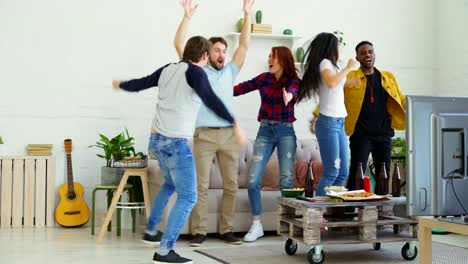 Glückliche-junge-Freunde-Sportspiel-im-Fernsehen-springen-und-feiern-Sieg-der-Lieblingsmannschaft-zu-Hause-beobachten