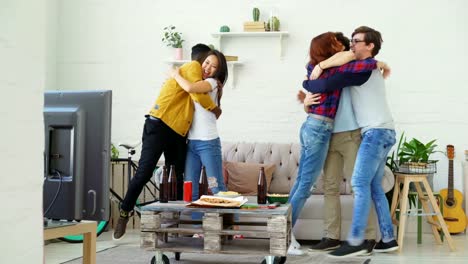 Football-fans-watching-sports-match-on-TV-sitting-on-couch-and-then-jumping-and-enjoying-victory-of-favourite-team-at-home