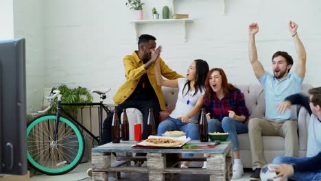 Amigos-jóvenes-felices-viendo-el-juego-de-deportes-en-la-TV-y-celebrando-la-victoria-del-equipo-favorito-en-casa