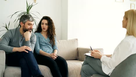 Pareja-joven-visita-la-oficina-del-profesional-psicólogo.-Mujer-rizada-airadamente-discutiendo-y-hablando-de-su-novio-para-consejero-de-matrimonio