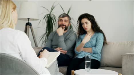 Close-up-of-professional-psychologist-writing-notes-and-listening-young-couple-who-arguing-and-talking-each-other