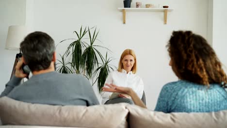 Weiblichen-professionellen-Psychologen-hören-und-Schreiben-von-Noten-in-Notebook-während-die-junge-Frau-streiten,-Freund-sprechen-per-Telefon-während-der-Besuch-Psychotherapie-Büro-im-Haus