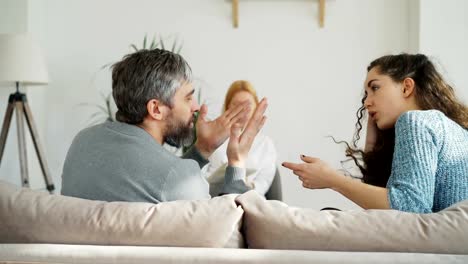 Mujer-psicoanalista-experimentado-escuchando-y-escribiendo-notas-mientras-que-enojado-matrimonio-argumentando-y-discutiendo-durante-visita-profesional-psicólogo-y-oficina-de-consejero-matrimonial