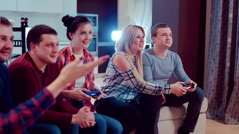 Compañía-de-los-amigos-de-relajarse-en-el-sofá-jugando-videojuegos-y-divirtiéndose-en-piso-moderno