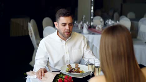 Young-couple-is-quarreling-while-dining-in-restaurant,-shouting-and-gesturing.-Bouquet-of-roses,-sparking-champagne-glasses-and-plates-with-food-are-visible.