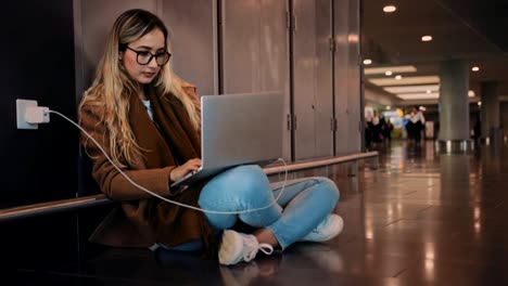 Young-woman-traveler-charging-laptop-and-working-at-airport