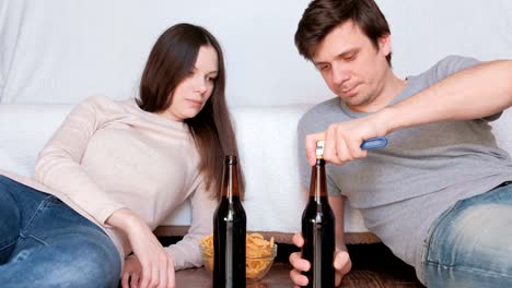 Appointment.-Couple-man-and-woman-lie-on-the-floor-at-home-eating-chips-and-drinking-beer.-Man-opens-beer-bottle.