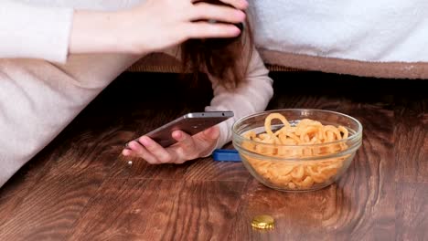 Mujer-joven-escribiendo-un-mensaje-en-el-móvil,-comer-patatas-fritas-y-bebiendo-cerveza.-Primer-plano-manos.