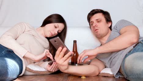 Couple-man-and-woman-browsing-internet-in-their-mobile-phones-drinking-beer-and-eating-chips-laying-on-the-floor.