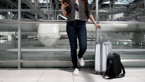 Close-up-woman-using-smart-phone-and-waiting-for-take-off-flight-with-luggage-and-baggage-at-airport.-People-and-lifestyles-concept.-Technology-and-trravel-theme.