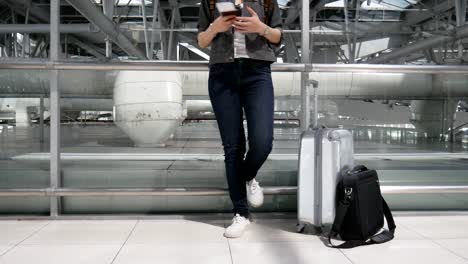 Close-up-woman-using-smart-phone-and-waiting-for-take-off-flight-with-luggage-and-baggage-at-airport.-People-and-lifestyles-concept.-Technology-and-trravel-theme.