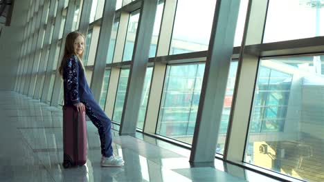 Adorable-little-girl-in-airport-near-big-window-playing-with-her-phone