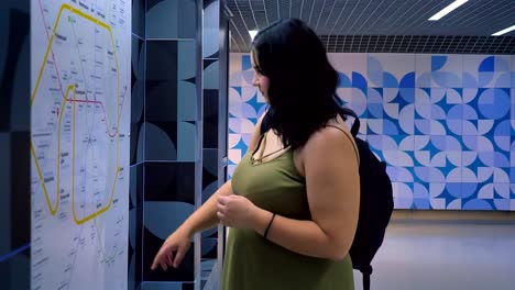 Beautiful-obese-woman-standing-in-modern-underground-subway-and-looking-at-map,-charming-female-tourist-with-backpack