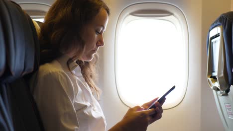 Woman-with-smarthone-sitting-in-airplane-near-window
