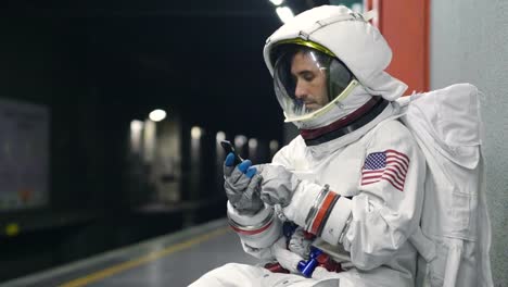 An-astronaut-dressed-man-uses-the-smartphone-to-call-and-send-messages.-The-astronaut-smiles-while-looking-at-the-phone-in-his-hand.