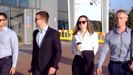 Group-of-young-business-person-walking-to-airport-at-sunny-day.-Colleagues-being-on-his-way-to-business-trip.-Business-people-going-to-terminal-and-talking.-Success-concept.-Slow-motion-Close-up