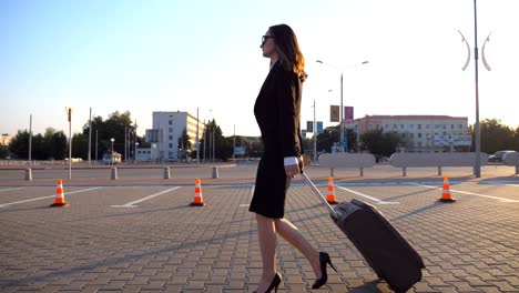 Young-businesswoman-going-to-taxi-parking-from-the-airport-with-her-suitcase.-Lady-walking-with-her-suitcase-along-street.-Travel-concept.-Side-view-Slow-motion-close-up