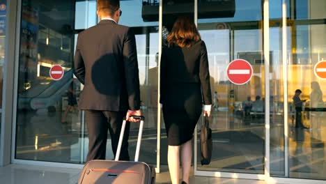 Hombre-de-negocios-y-de-la-mujer-al-aeropuerto-con-su-equipaje.-Joven-empresario-llevar-maleta-de-ruedas-y-caminar-con-su-colega-al-pasillo-de-la-terminal.-Concepto-de-viaje-o-viaje.-Vista-posterior