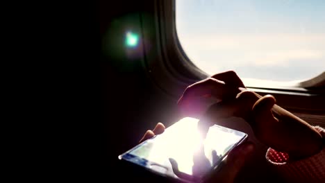 Close-up.-los-rayos-del-sol-se-reflejan-en-el-teléfono.-silueta-oscura-de-las-manos-del-niño-y-el-teléfono-móvil-contra-iluminador-del-avión.-Niño-con,-juego-de-juegos-en-smartphone,-teléfono-tableta-en-cabina-de-avión