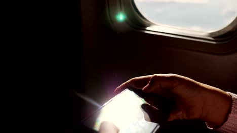 Close-up.-los-rayos-del-sol-se-reflejan-en-el-teléfono.-silueta-oscura-de-las-manos-del-niño-y-el-teléfono-móvil-contra-iluminador-del-avión.-Niño-con,-juego-de-juegos-en-smartphone,-teléfono-tableta-en-cabina-de-avión