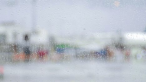 Raindrops-fall-on-airport-window-as-planes-bus-past