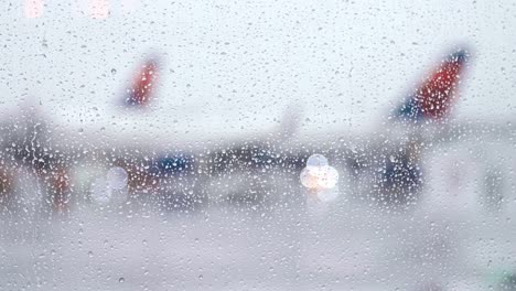 Regentropfen-fallen-auf-hellen-Fenster-als-Flugzeug-Taxis-auf-Asphalt-an-regnerischen-Tag