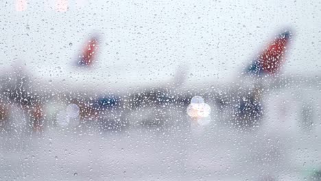 Raindrops-fall-on-bright-window-as-airplane-taxis-along-tarmac-on-rainy-day