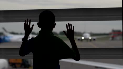 niño-encuentra-cerca-de-la-ventana-en-el-aeropuerto-y-se-ve-en-los-planos,-el-niño-sueña-con-ser-un-piloto