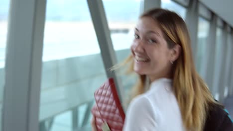 Young-handsome-woman-smiling-looking-at-camera-and-going-to-boarding-plane-at-the-airport-terminal