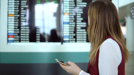 Triste-mujer-joven-era-tarde-para-el-avión-y-se-encuentra-en-el-fondo-del-marcador-borrosa-con-el-aviso-y-mira-y-mecanografiar-en-el-smartphone.