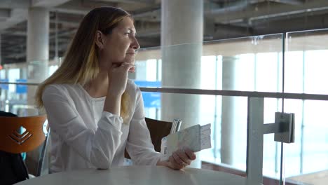 Young-beautiful-girl-sits-at-table-with-ticket-and-waits-for-airplane.