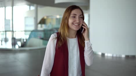 Positive-young-girl-in-elegant-clothes-speaks-on-smartphone-at-the-airport