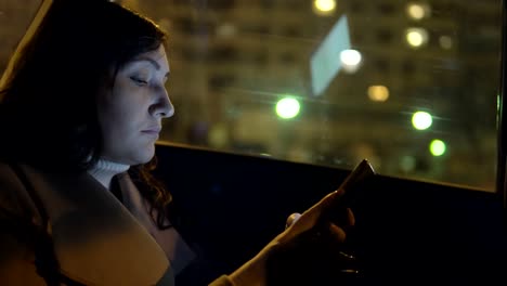 Mujer-joven-en-el-asiento-del-copiloto-de-un-coche-con-un-teléfono-con-paseos-por-la-ciudad-de-noche