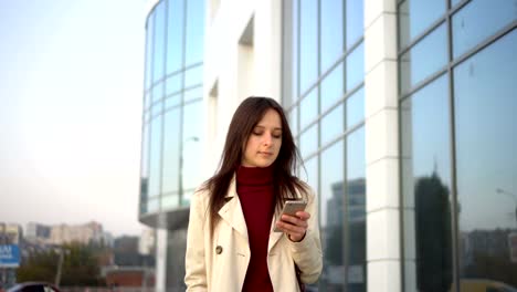 A-beautiful-girl-uses-her-phone-and-walks-along-the-city-street-in-the-evening.