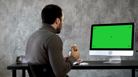 Business-man-in-the-office-having-breakfast,-lunch-and-watching-something-on-the-mac,-computer.-Green-Screen-Mock-up-Display