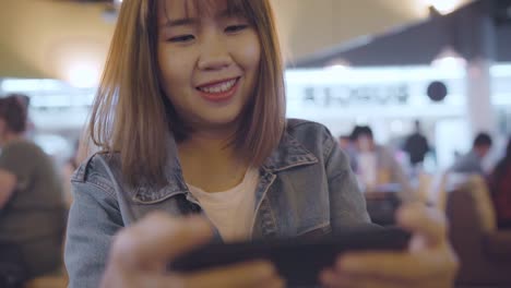 Happy-Asian-woman-using-and-checking-her-smartphone-while-sitting-on-chair-in-terminal-hall-while-waiting-her-flight-at-the-departure-gate-in-international-airport.-Women-happy-in-airport-concept.