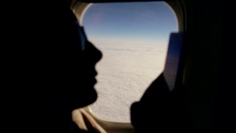 Closeup-silhouette-woman-sitting-near-airplane-window-using-mobile-phone-during-flight