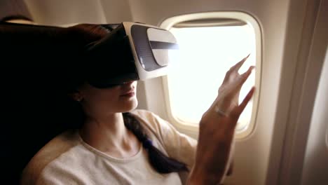 Junge-Touristen-Frau-entspannen-und-mit-VR-Kopfhörer-für-Smartphone-während-des-Fluges-im-Flugzeug