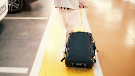 Young-stylish-female-traveler-walking-across-the-airport-parking-place-with-suitcase.-Girl-come-on-vacation