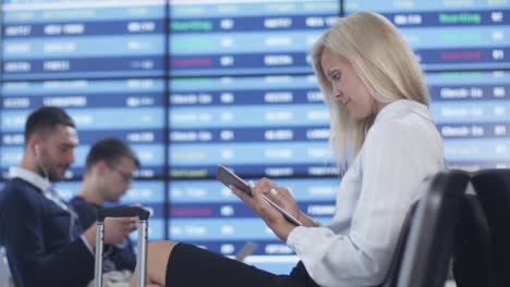 Attraktive-Adult-Business-Frau-mit-Tablet-PC-beim-Boarding-warten-am-Abflug-Lounge-am-Flughafen.